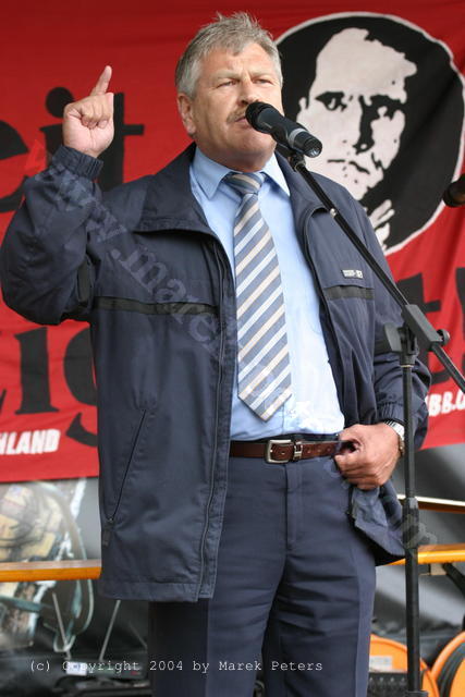 NPD-Parteivorsitzender Udo Voigt mit erhobenem Zeigefinger vor Konterfei von Rudolf Hess
