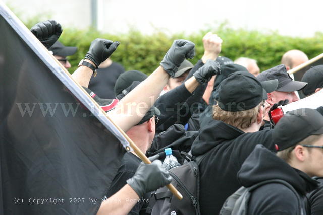 Autonome Nationalisten mit erhobenen Fäusten mit schwarzer Fahne und Handschuhen