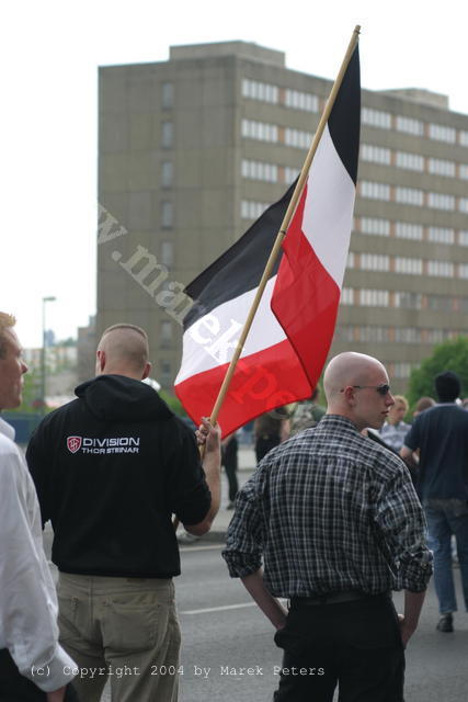Skinheads mit Pullover "Division Thor Steinar" mit schwarz-weiss-roter Fahne vor Plattenbau-Hochhaus